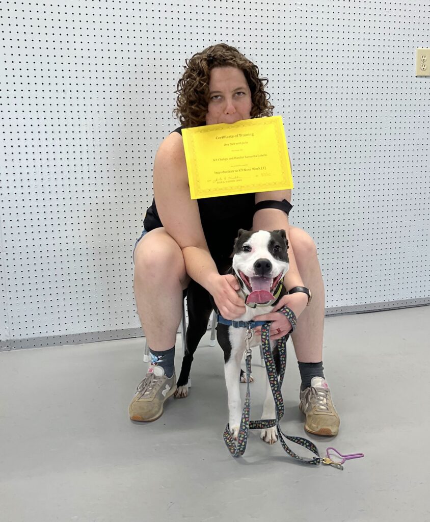 A woman holding a certificate in her mouth and posing with a dog