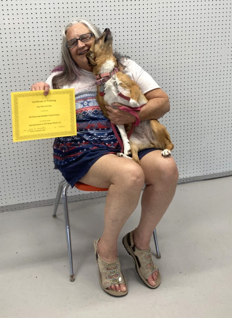 A woman sitting with a dog on her lap and showing a yellow colored certificate