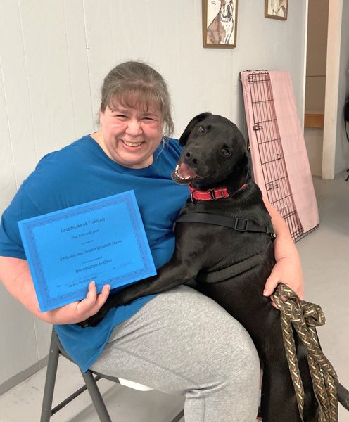 A woman with a black dog holding a certificate.