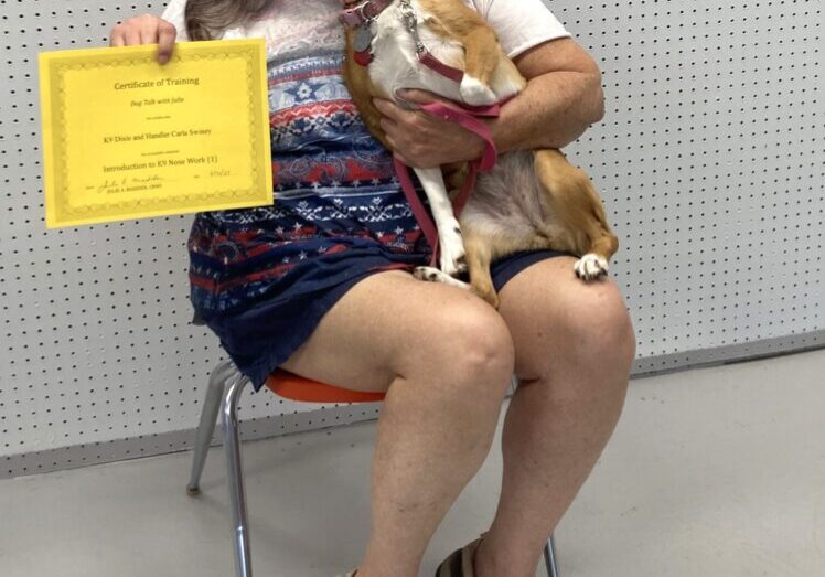 A woman sitting with a dog on her lap and showing a yellow colored certificate