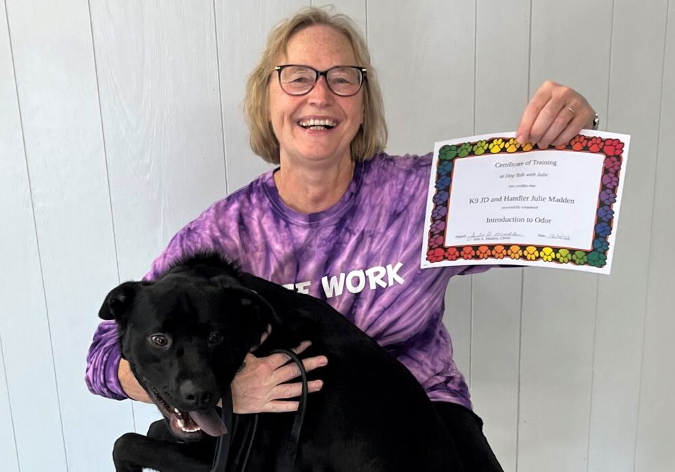 A woman holding a certificate and her dog on her lap